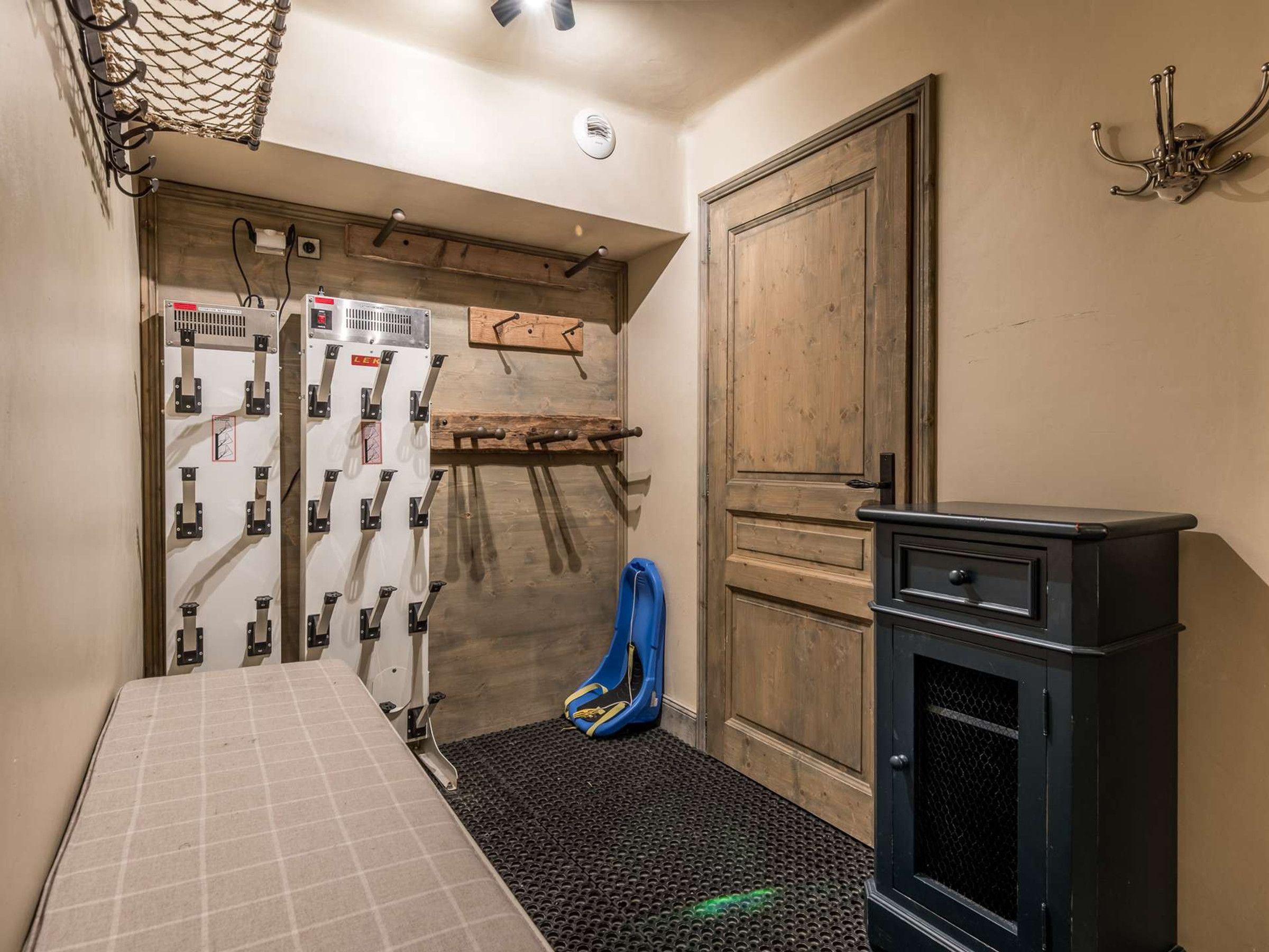 Una habitación pequeña con cama, un mueble negro, una puerta de madera y un soporte en la pared con herramientas.