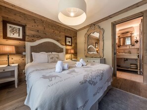 Ein Schlafzimmer mit Holzwandverkleidung, einem Bett, Nachttischlampen, einem Spiegel und einem durchgegangenen Tür sichtbar erkennbaren Badezimmer.