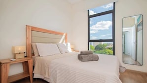 A bedroom with a large window, a bed with a wooden headboard, a bedside table with a lamp, and a mirror on the wall. - Corporate Stays Spirit Villa Morra (Asunción)