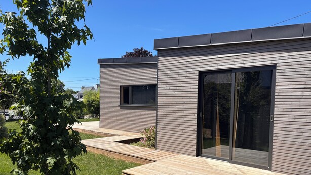 Ein modernes Haus mit einer Holzterrasse, einer großen Glasschiebetür und einem kleinen Fenster.