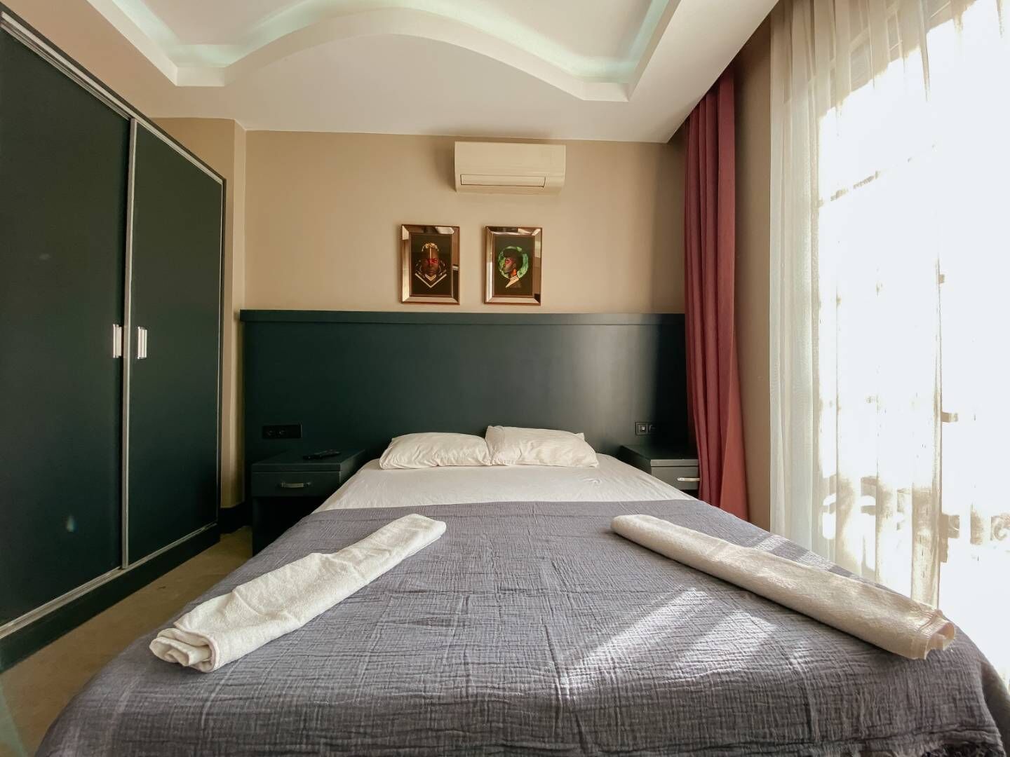 A hotel room with a bed, a wardrobe, two framed pictures, and a window with curtains.