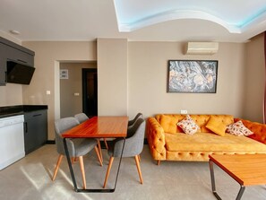 Una sala de estar moderna con un sofá, una mesa de comedor y sillas. Incluye una zona de cocina con estufa y televisión.