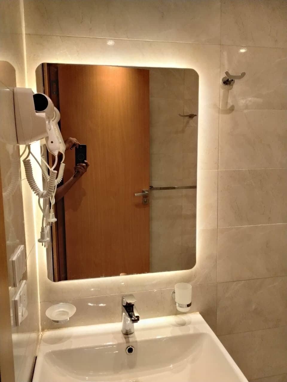 Une salle de bain avec un grand miroir, un sèche-cheveux, un lavabo et une porte en bois.