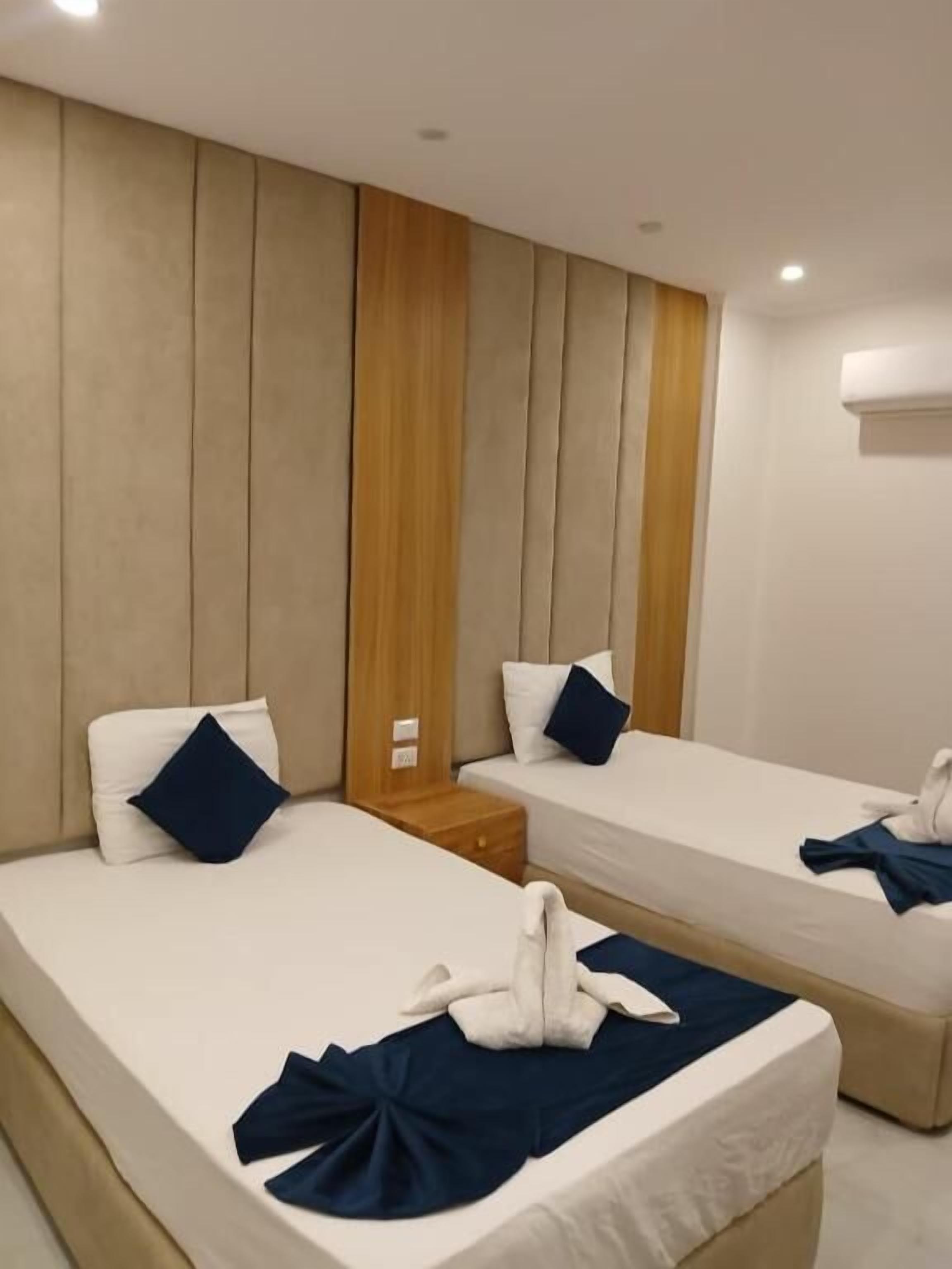 A hotel room with two single beds, a wooden accent wall, and a small bedside table.
