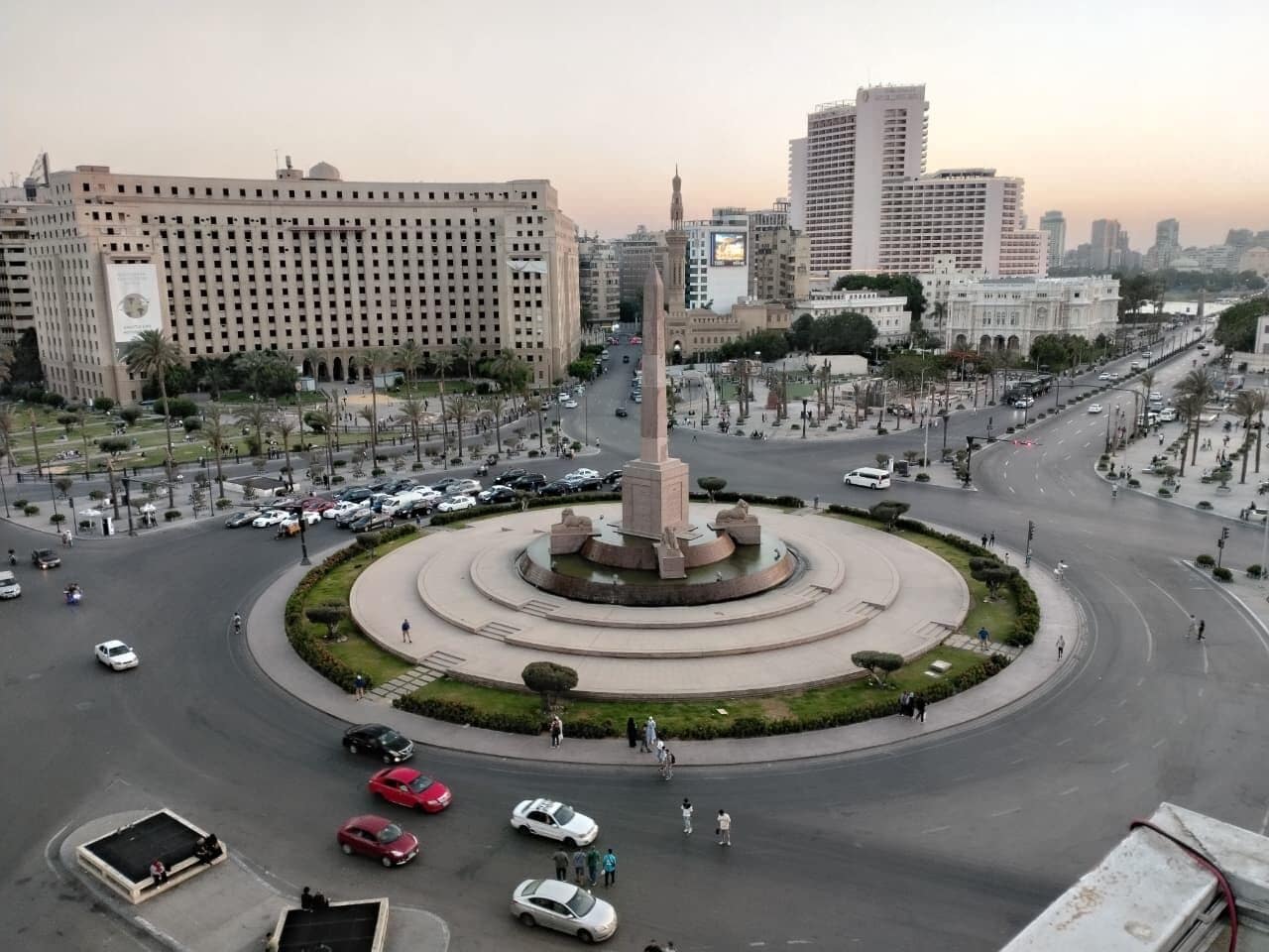Una glorieta con un monumento central, rodeada de edificios y una calle con mucho tráfico.