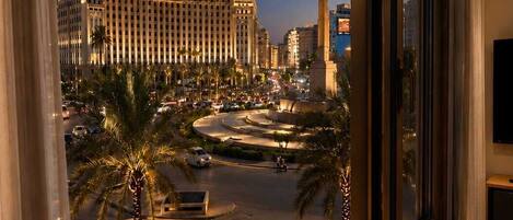 A view from a hotel room window overlooking a cityscape with a large building, palm trees, and a monument.