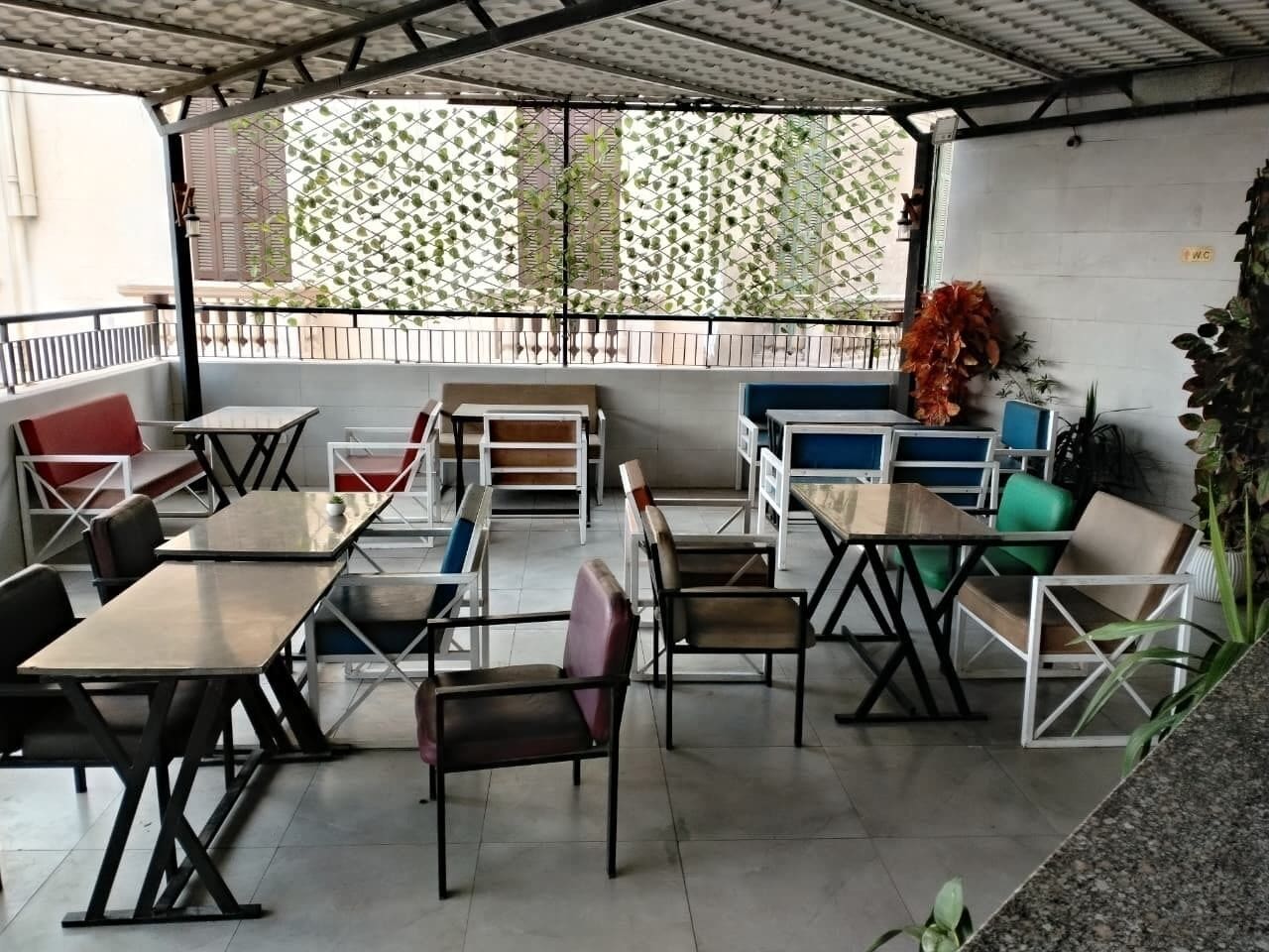 Un espacio al aire libre con mesas y sillas, una zona cubierta y vista a la calle.