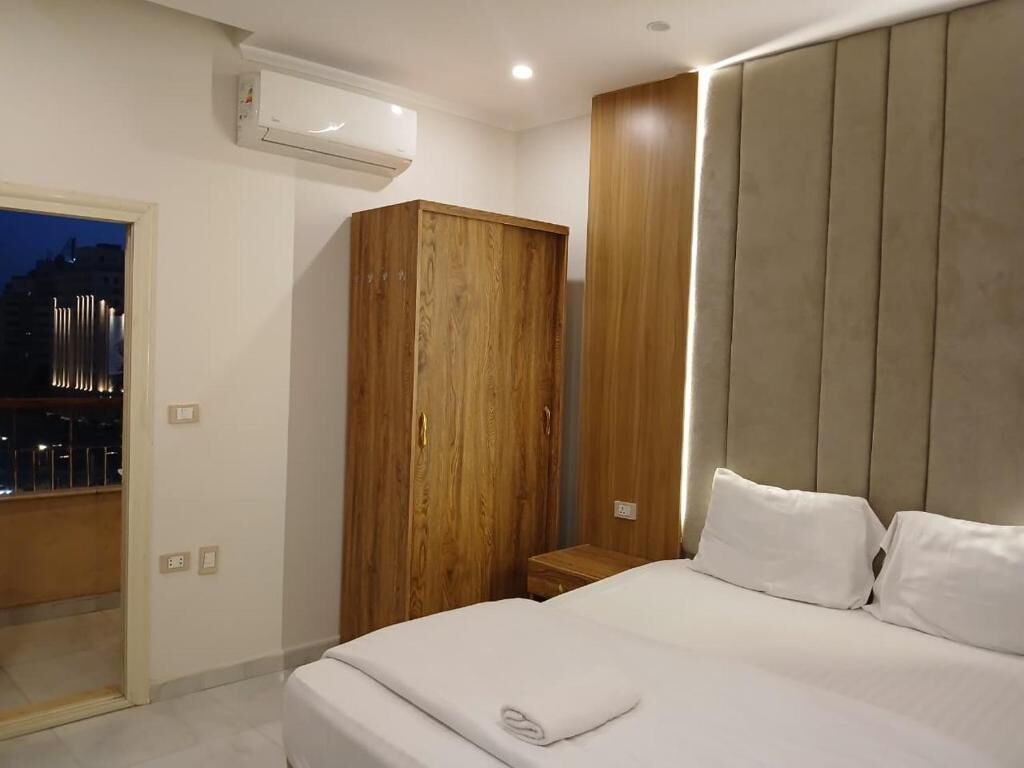 A bedroom with a bed, a wooden wardrobe, a nightstand, and an air conditioning unit.