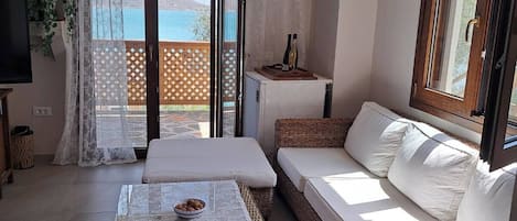 Une chambre avec un lit, un canapé, une table recouverte d’une nappe en dentelle, un téléviseur et une vue sur la mer.