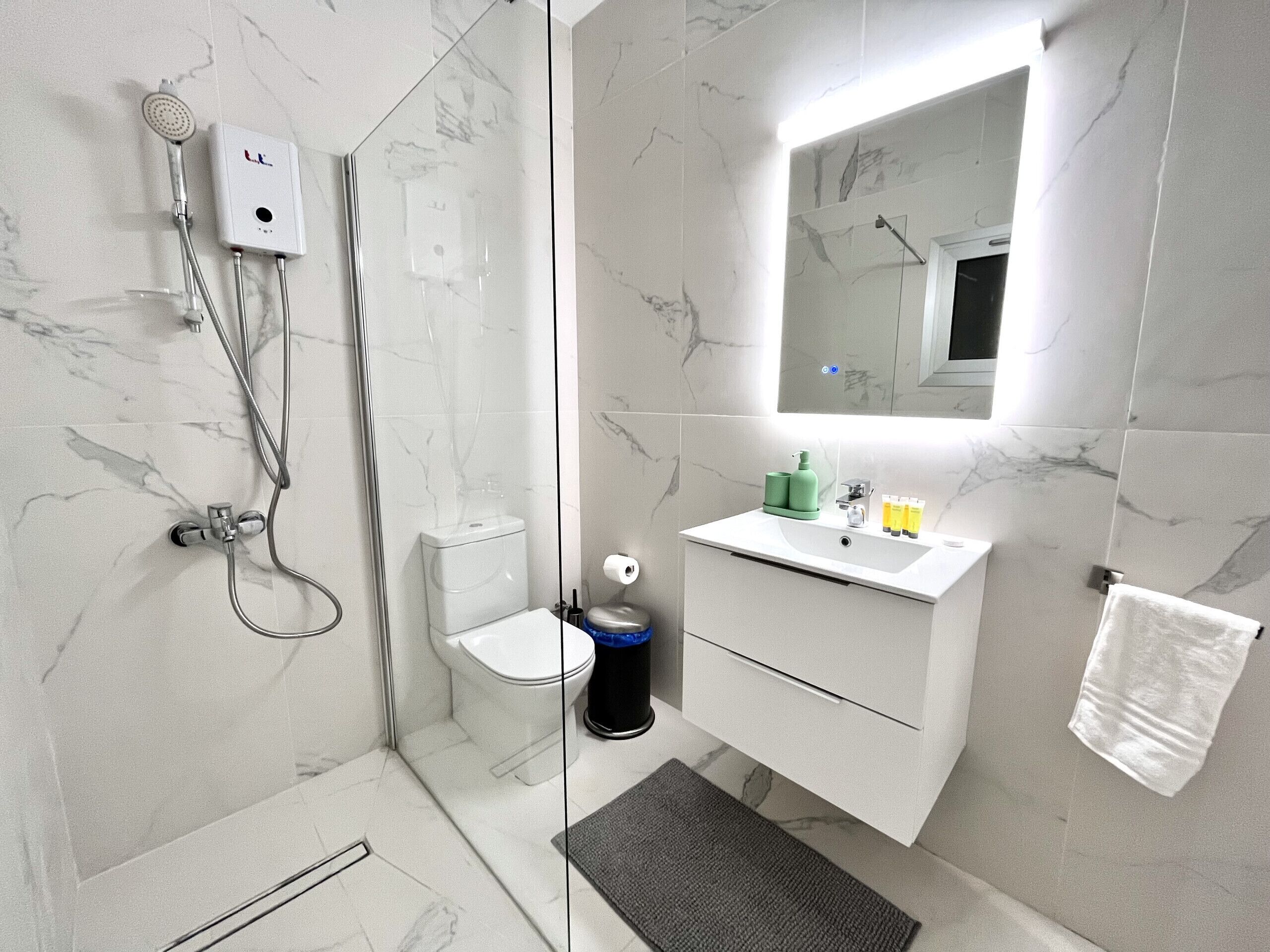 Ett modernt badrum med en dusch som är avskärmad med glasväggar, en toalett, ett handfat med tillhörande hygienartiklar och en spegel ovanför handfatet.