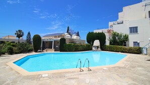 Une piscine dotée d’une plage en pierre, entourée de verdure et de bâtiments.