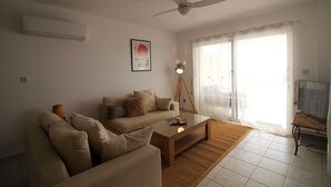 Un salon comprenant un canapé, une table basse, un ventilateur de plafond et une grande fenêtre avec des rideaux.