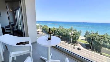 Een balkon met een ronde tafel, twee witte stoelen, een fles wijn en uitzicht op zee en groen.