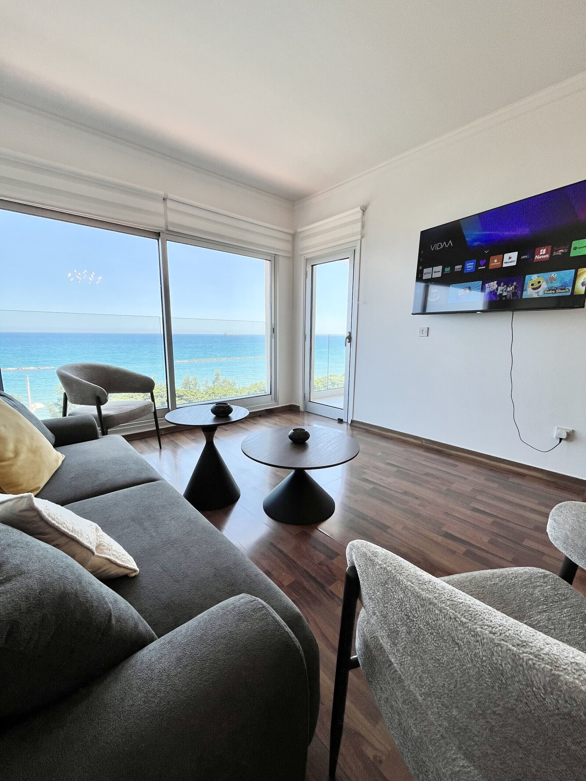 Een moderne woonkamer met een grote televisie, comfortabele zithoek en uitzicht op zee.