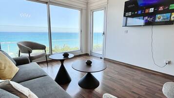 Een moderne woonkamer met een grote televisie, comfortabele zithoek en uitzicht op zee.