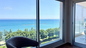 Habitación con amplia ventana que ofrece vista al mar, una silla y balcón con mesa.
