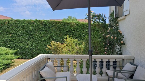 A balcony with outdoor furniture, a large umbrella, and a view of a hedge and building. - House with a pool; 4 bedrooms, including 2 with double beds (Chassey-le-Camp)
