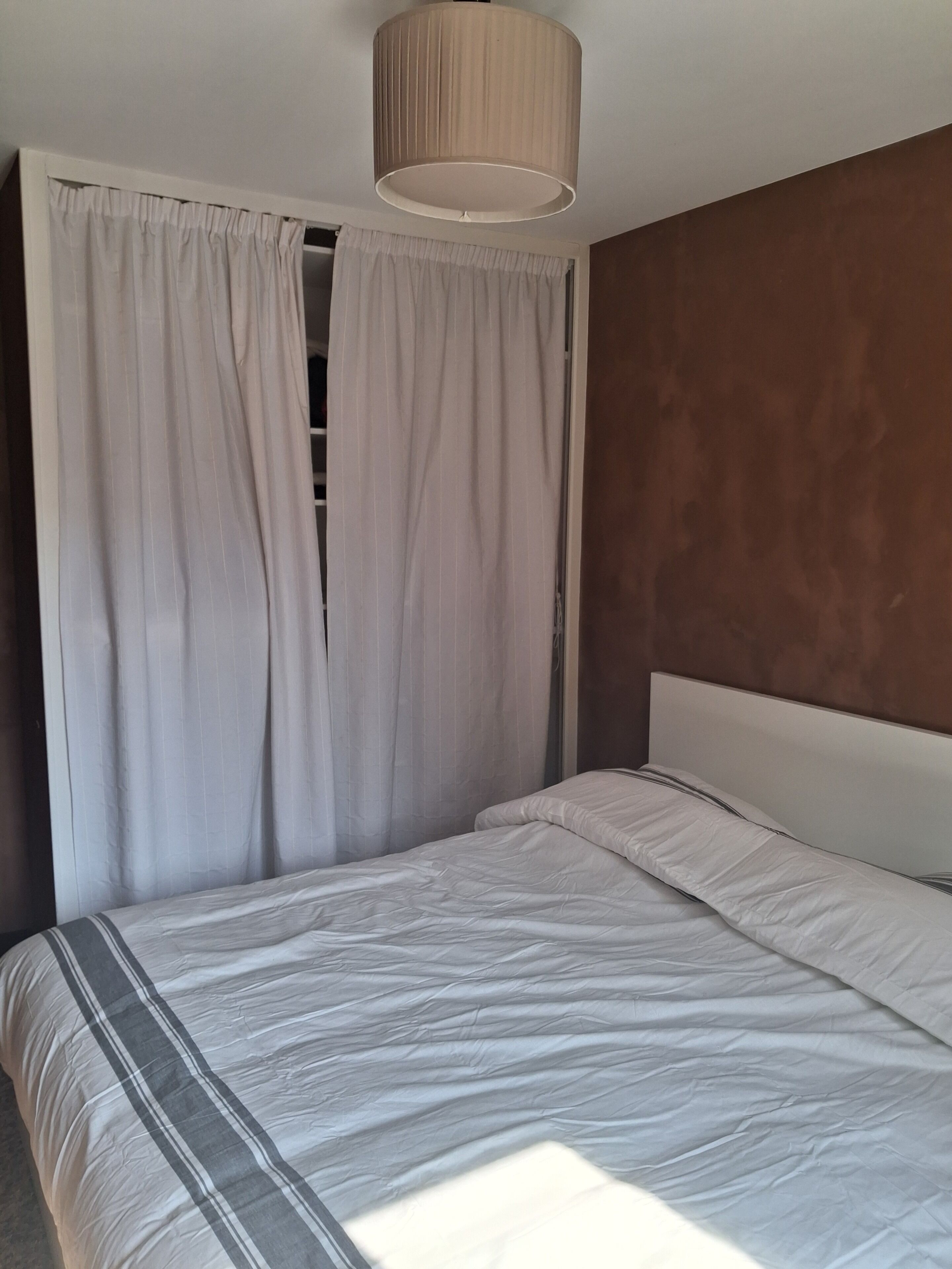 Un dormitorio con cama, cortinas y lámpara en el techo.