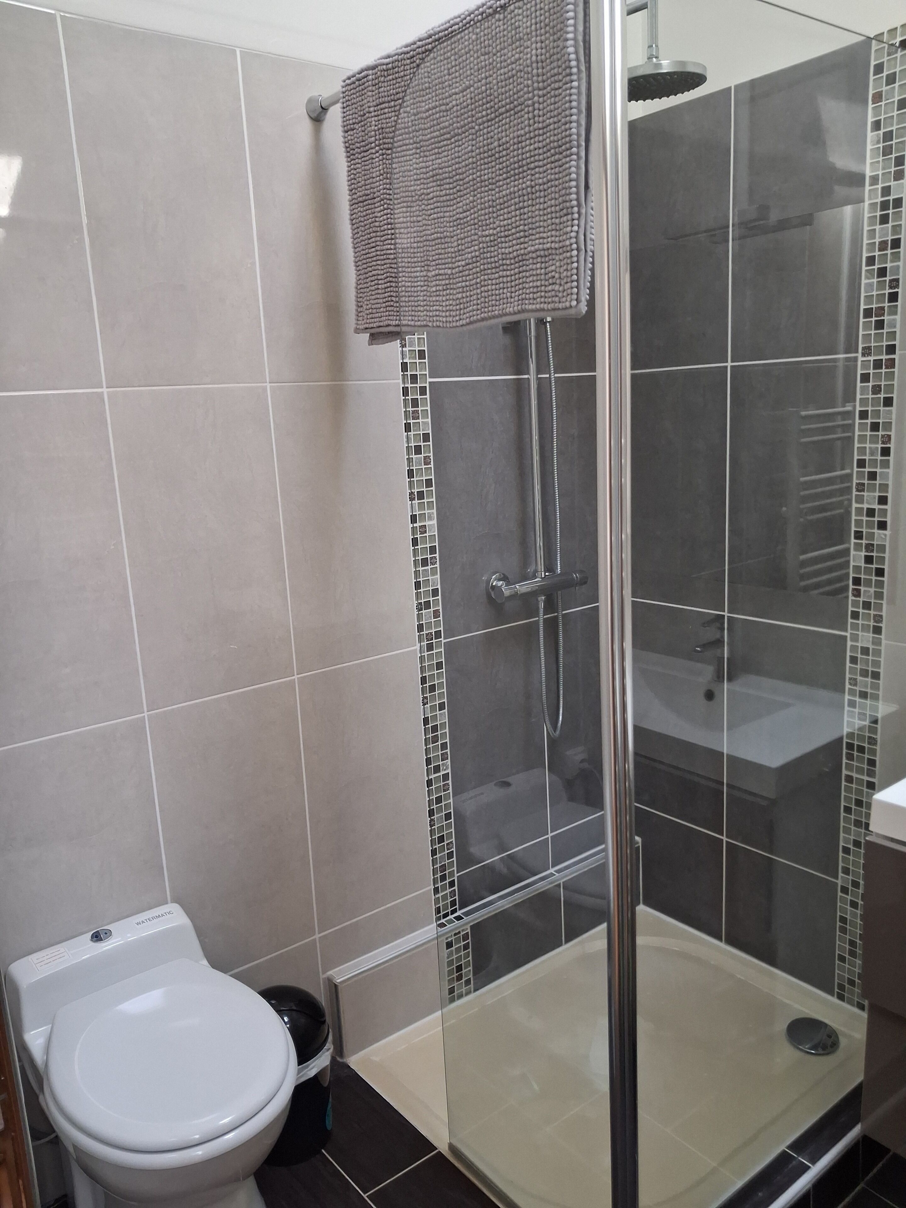 Une salle de bain moderne avec une douche à parois de verre, des toilettes blanches et des murs carrelés.