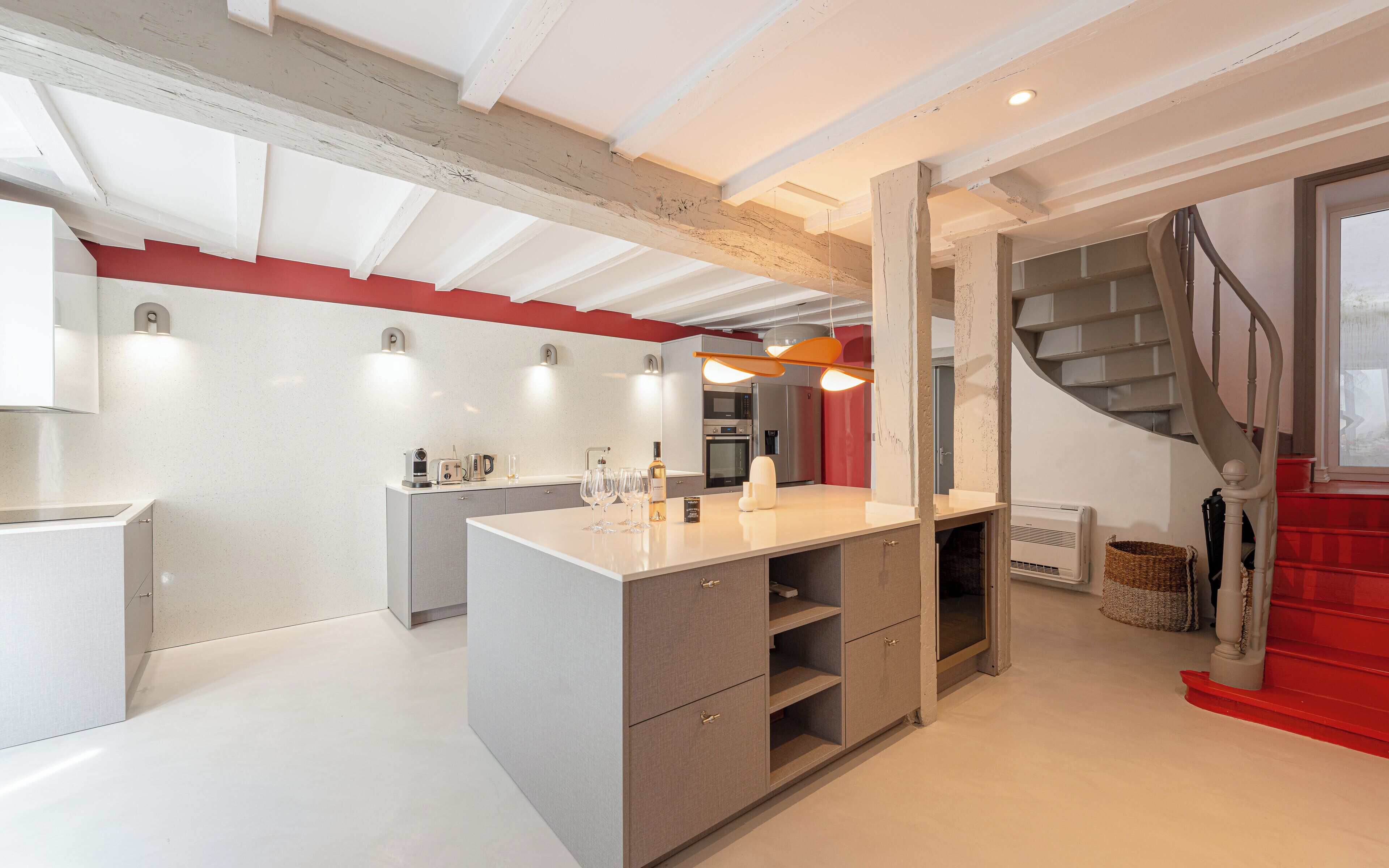Una cocina moderna con una isla central, electrodomésticos integrados y una escalera que lleva a un rellano rojo.