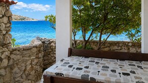A balcony with a stone wall, a wooden bench, and a table with a patterned tablecloth. - 1 bedroom beach front apartment in Smokvica (Smokvica)