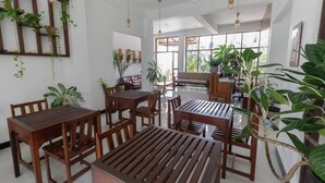 Un comedor amplio con mesas y sillas de madera, rodeado de ventanas grandes y plantas en macetas.