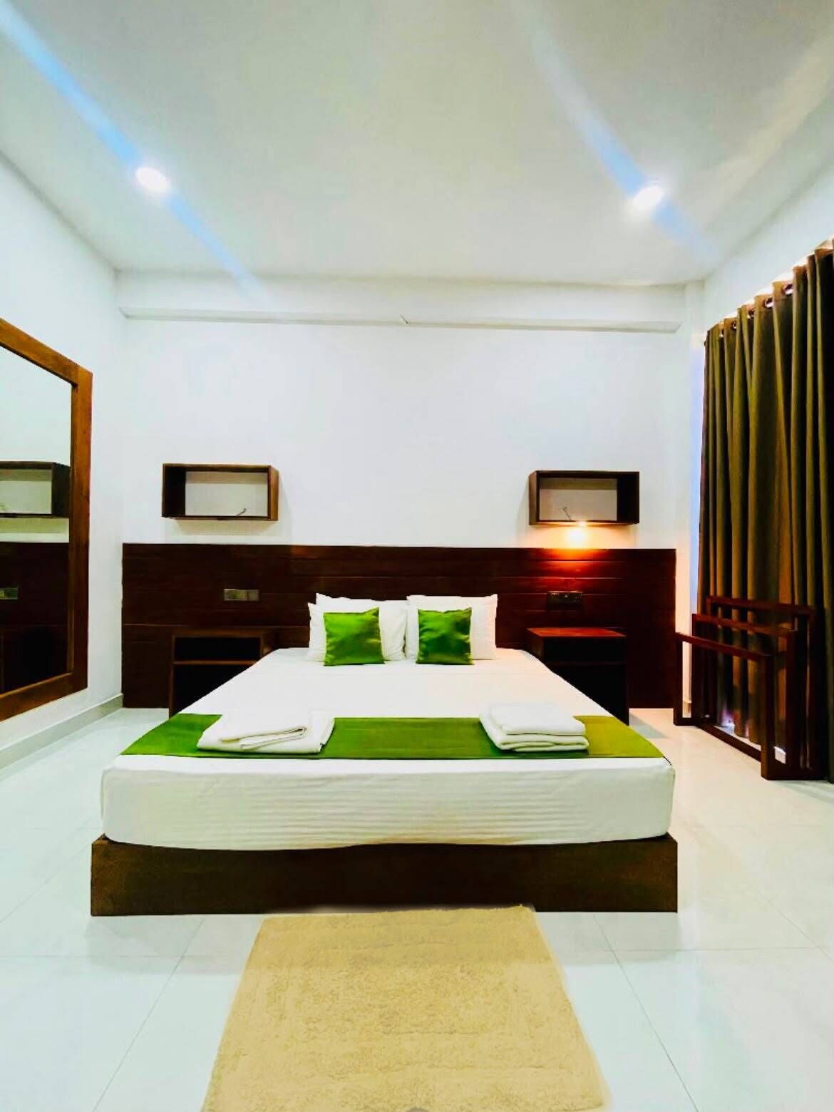 A modern hotel room with a large bed, a wooden headboard, a nightstand, a mirror, and a curtain.