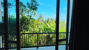Una habitación con un amplio ventanal corredero que da a un balcón con vistas a zonas verdes y un cielo despejado.