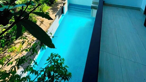 Un área de piscina con cielo azul despejado, pared blanca y vegetación tropical.