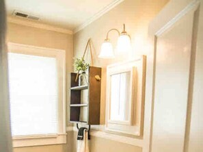 Ein Badezimmer mit Fenster, Ablagefläche mit Pflanze und Wandleuchten.