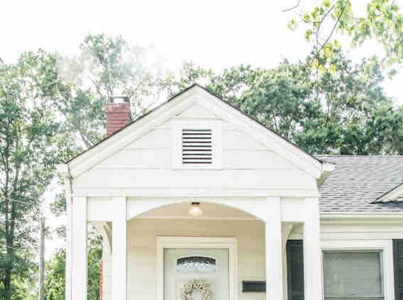 A white building with a gabled roof, a front door, and a small porch.
