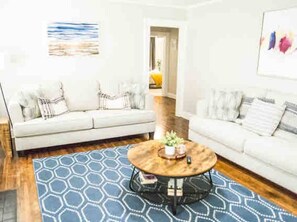 Ein Wohnzimmer mit zwei weißen Sofas, einem runden Couchtisch und einem blau gemusterten Teppich.