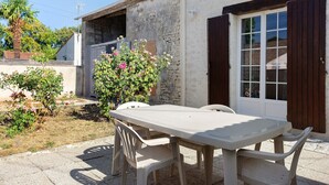 A patio with a table and chairs, a stone wall, and a door with wooden shutters. - Country House “La Demeure D'Elles” with Private Terrace and Garden (Le Thou)