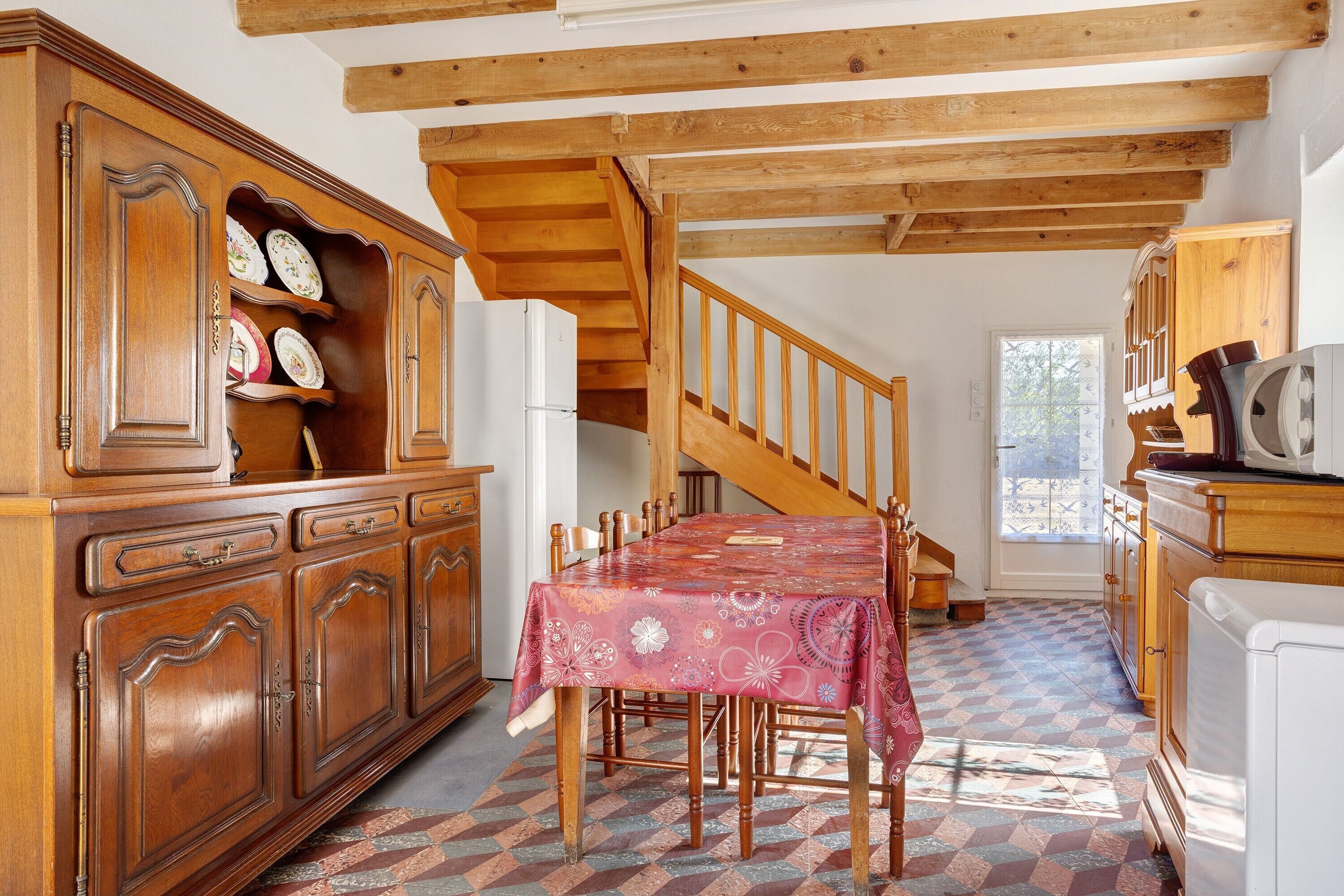 A kitchen with wooden cabinets, a dining table, and a staircase.
