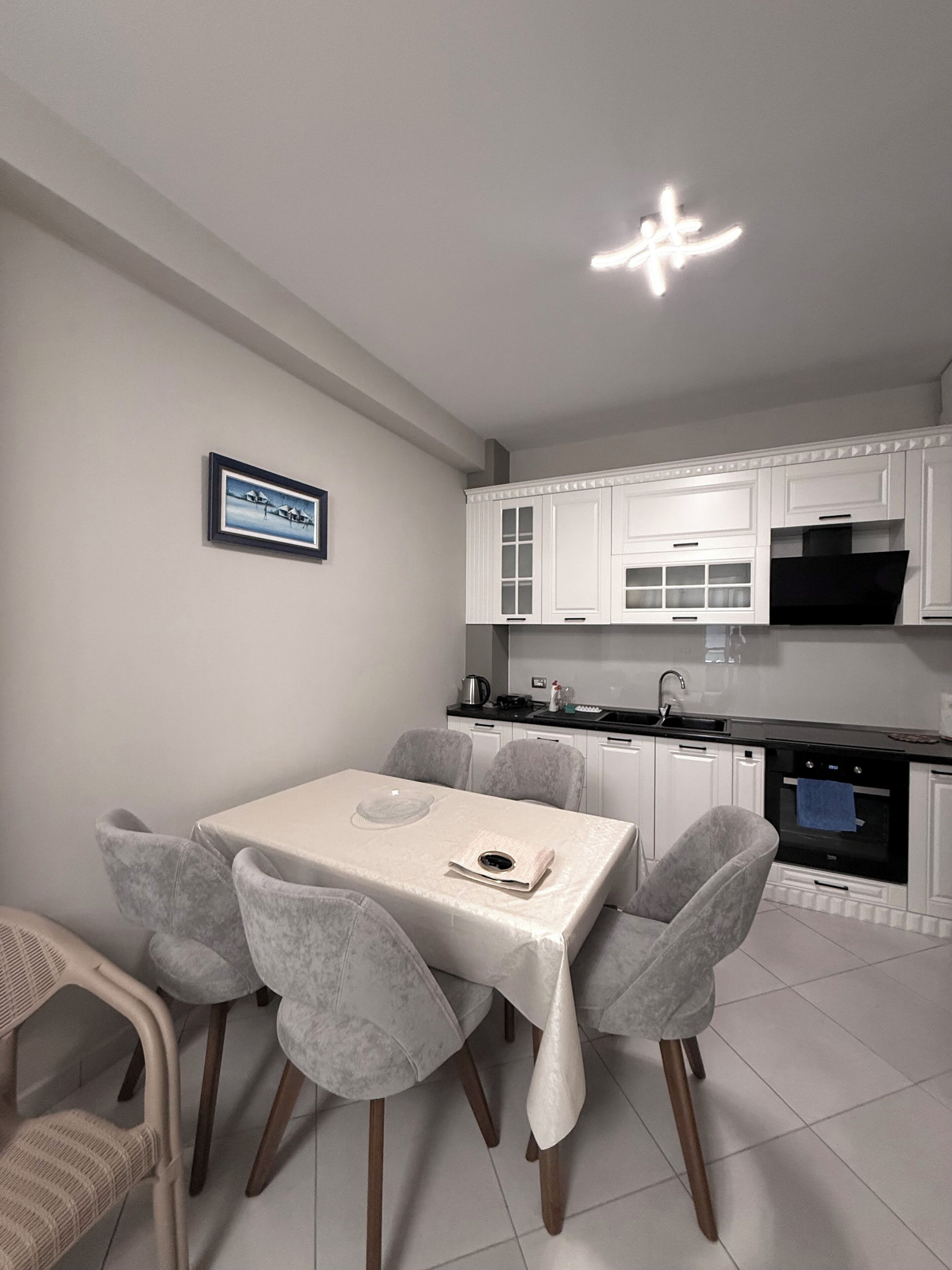 A modern kitchen with white cabinets, a dining table with chairs, and a framed picture on the wall.