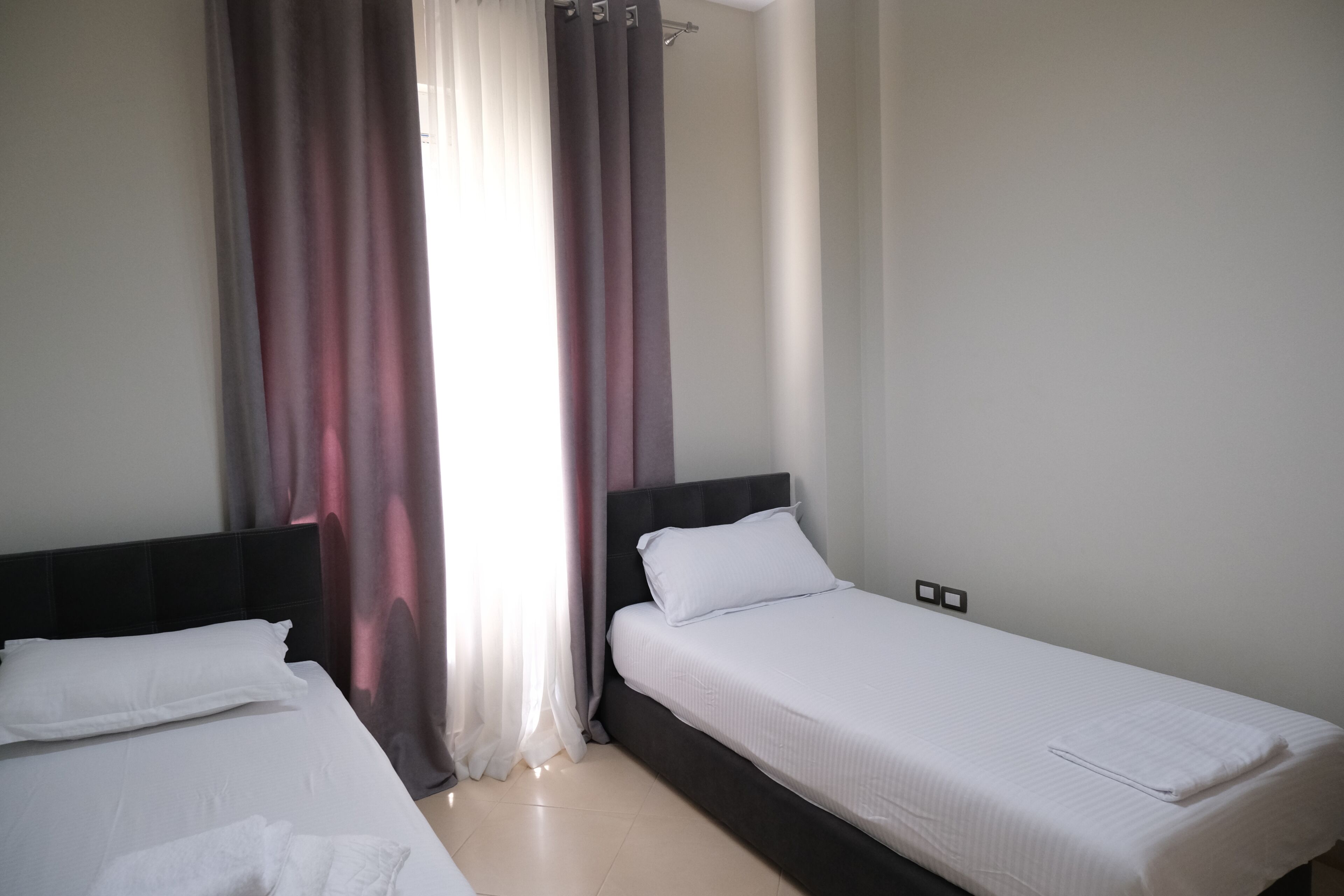 Una habitación de hotel con dos camas individuales, una ventana con cortinas y un suelo de color claro.