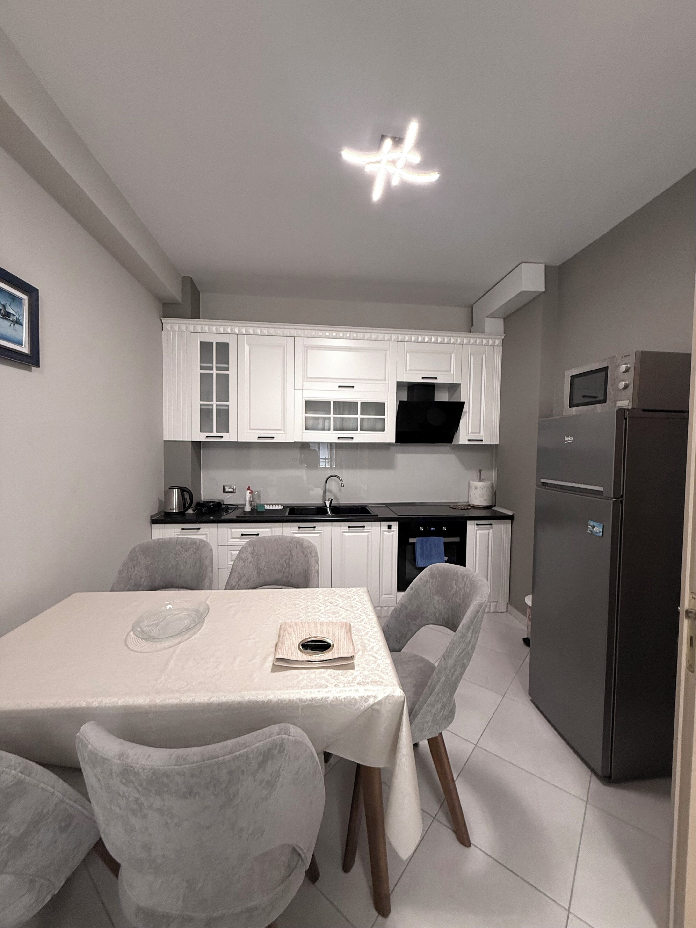 A modern kitchen with white cabinets, a black countertop, a stainless steel refrigerator, and a dining area with a table and chairs.