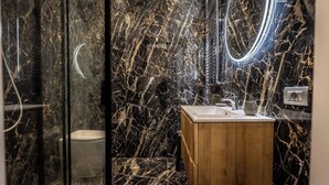 Une salle de bain avec un mur en marbre, un meuble-lavabo en bois, des toilettes et un miroir avec un éclairage intégré.