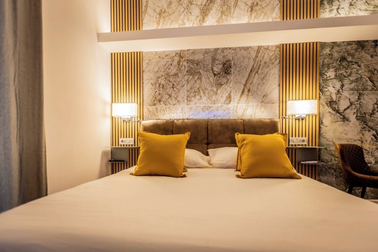 Habitació d'hotel amb un llit gran, dues làmpades de nit, un frontal de marbre i un panell de paret de fusta.