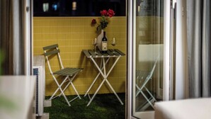 Un petit espace extérieur aménagé avec une table, deux chaises, une bouteille de vin et un vase de fleurs.