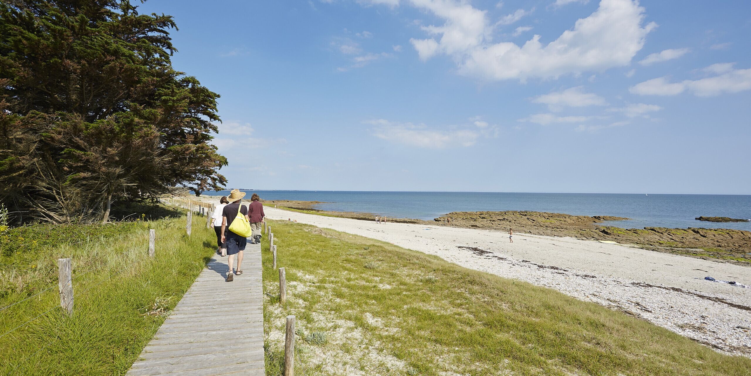 A wooden boardwalk leading to a beach with a clear sky and calm sea.