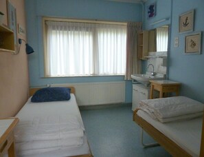 Ein Zimmer mit zwei Betten, einem Fenster mit Vorhängen, einem Waschbecken und einem Spiegel.