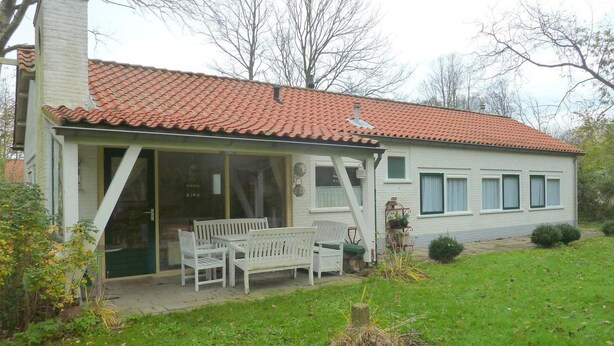 A single-story house with a tiled roof, a covered porch with white furniture, and a small garden area. - Family Bungalow With Enclosed Garden (Koudekerke)