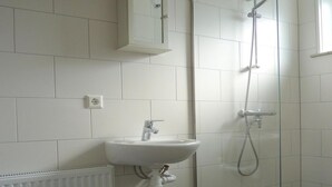 A bathroom with a white sink, a glass shower enclosure, and a white tiled wall. - Family Bungalow With Enclosed Garden (Koudekerke)