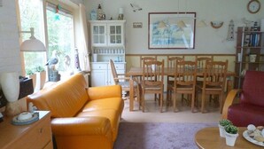A living room with a sofa, dining table, chairs, a bookshelf, and a painting on the wall. - Family Bungalow With Enclosed Garden (Koudekerke)