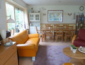Ein Wohnzimmer mit einer Couch, einem Esstisch, Stühlen, einem Bücherregal und einem Bild an der Wand.
