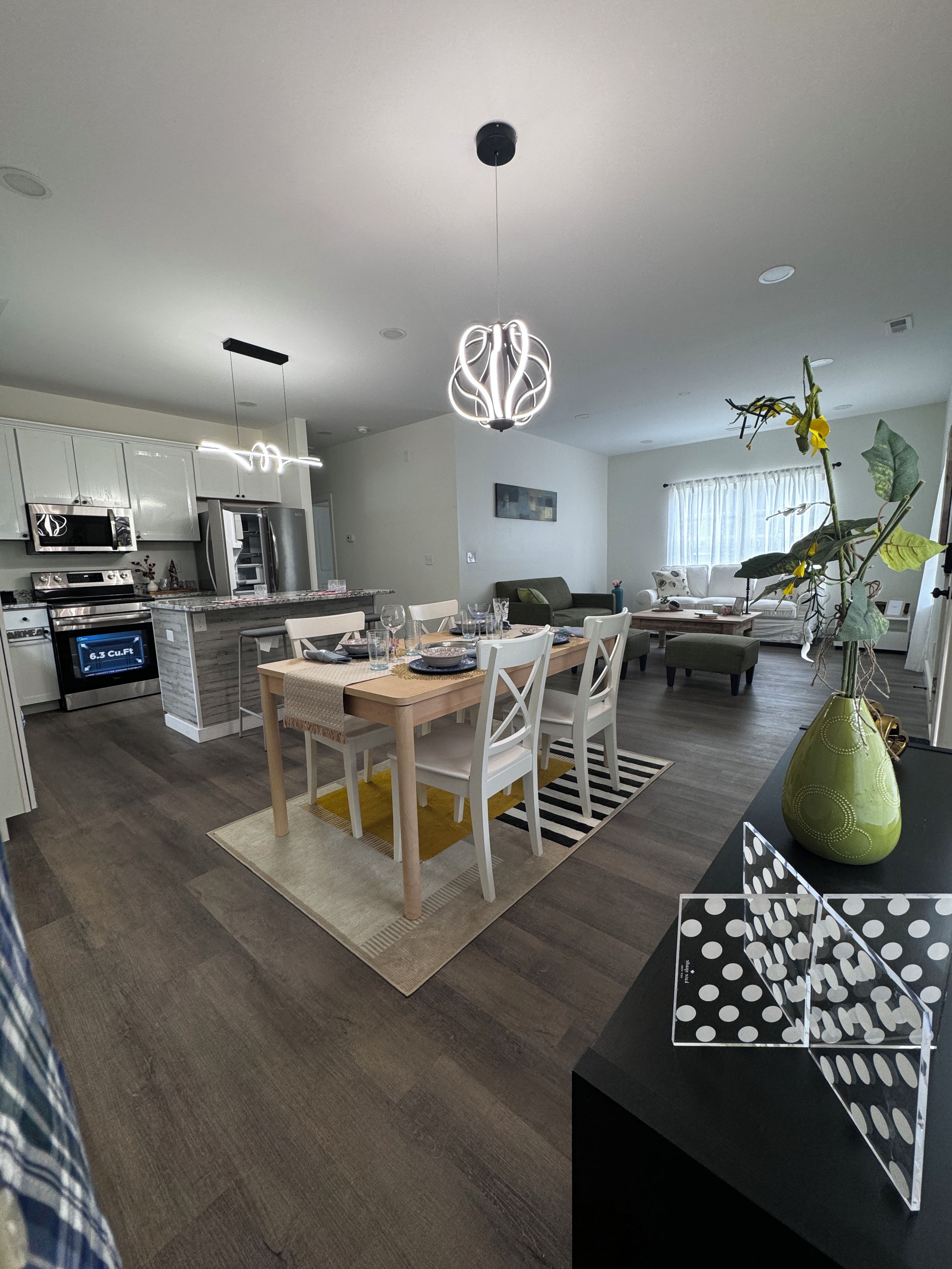 A modern kitchen with built-in appliances, a dining area with a wooden table and white chairs, and a living room with a sofa and a coffee table.
