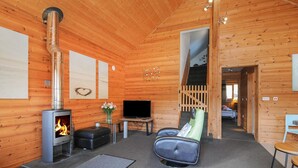 A wooden cabin interior with a fireplace, a television, a sofa, and a chair. - Trevano (Bodmin)