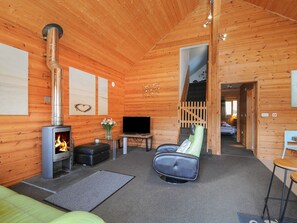 A wooden cabin interior with a fireplace, a television, a sofa, and a chair. - Trevano (Bodmin)