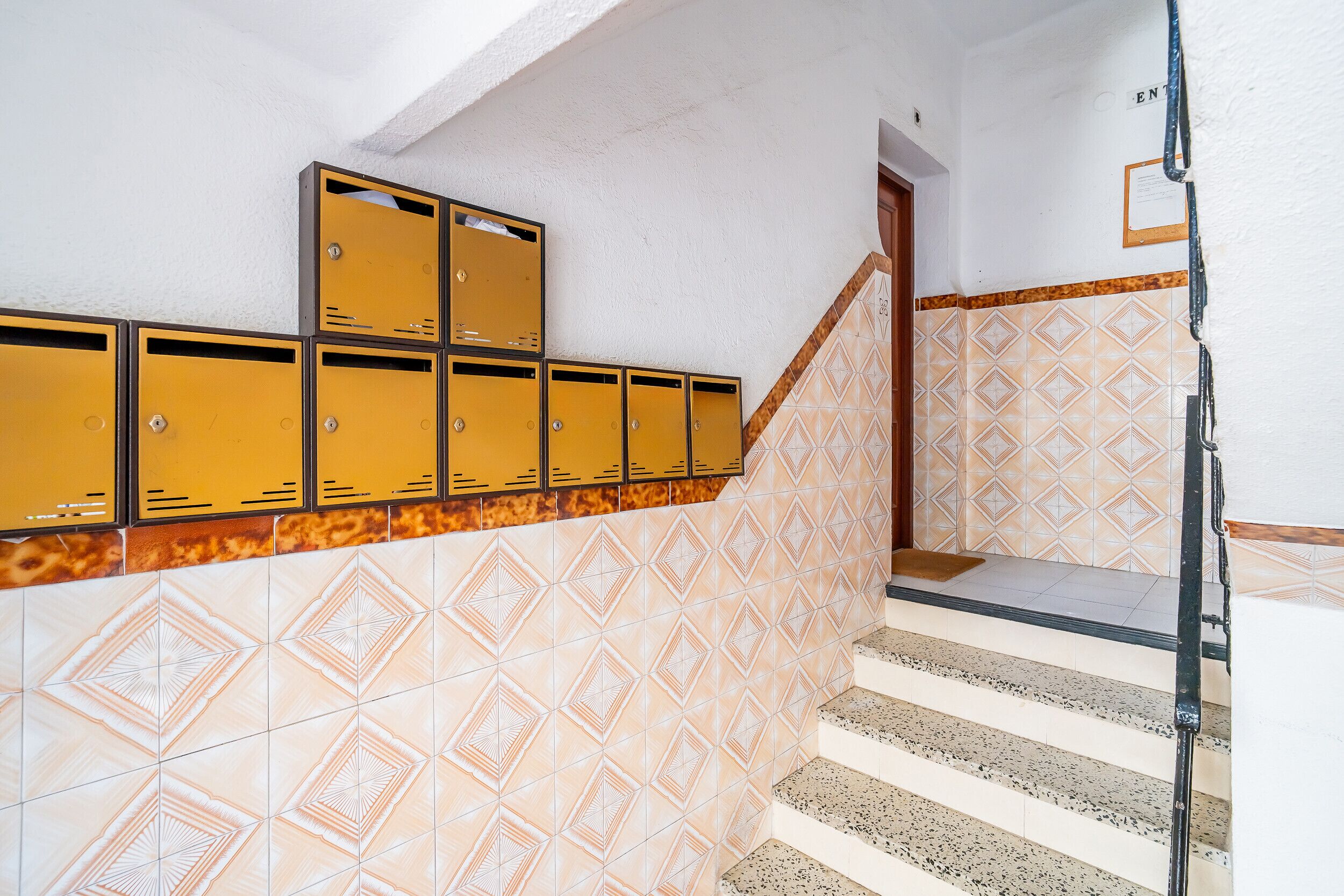 Un escalier avec un mur orné de motifs, une rampe métallique et une porte sur laquelle est fixée une enseigne.